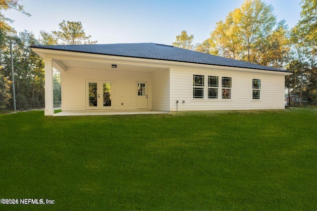 rear view of house with a shingled roof, a patio, a lawn, and french doors