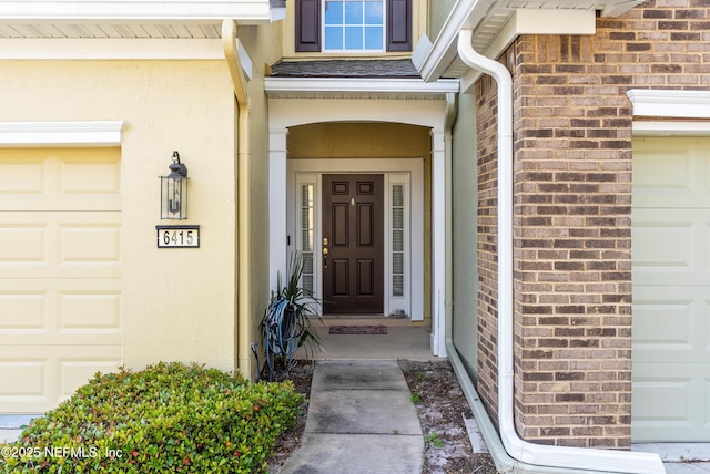 view of exterior entry with a garage, stucco siding, and brick siding