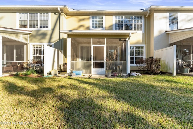 back of house featuring a sunroom, a lawn, and stucco siding