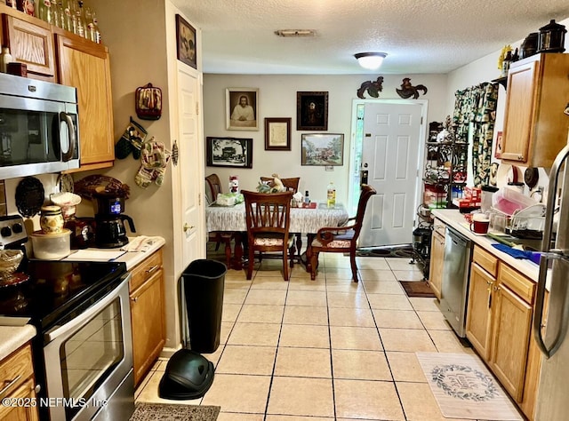 kitchen featuring light tile patterned floors, light countertops, appliances with stainless steel finishes, brown cabinetry, and a textured ceiling