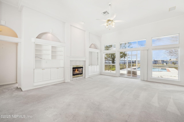 unfurnished living room featuring built in features, visible vents, a towering ceiling, light carpet, and a tile fireplace