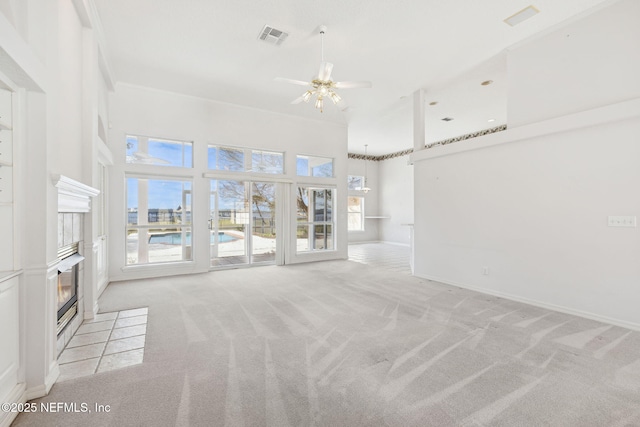 unfurnished living room featuring a fireplace, visible vents, a high ceiling, light carpet, and ceiling fan