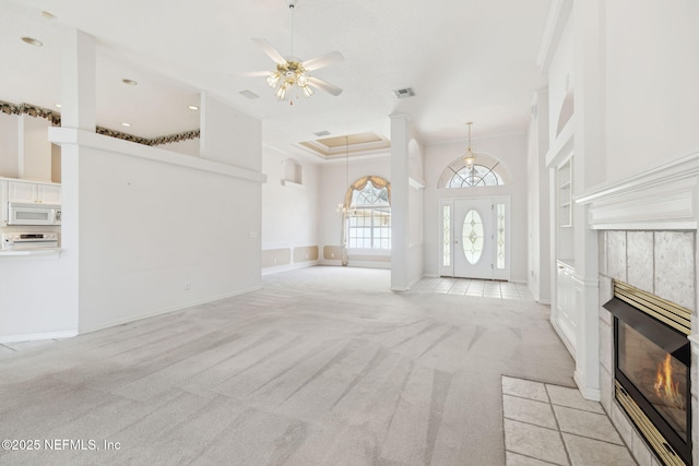 unfurnished living room featuring a tile fireplace, light carpet, visible vents, a towering ceiling, and baseboards