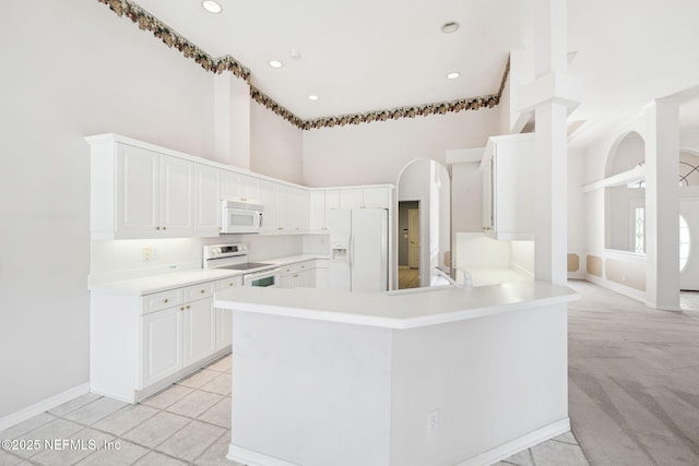 kitchen featuring white appliances, a towering ceiling, a peninsula, light countertops, and white cabinetry