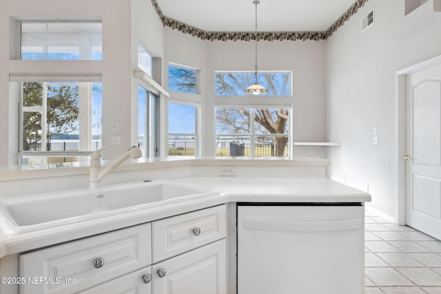 kitchen with visible vents, white cabinets, hanging light fixtures, white dishwasher, and a sink