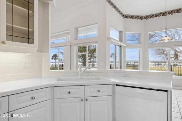 kitchen featuring white dishwasher, a sink, glass insert cabinets, and white cabinets