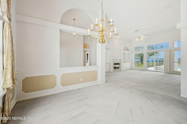 unfurnished living room with a high ceiling, a tiled fireplace, carpet flooring, baseboards, and ceiling fan with notable chandelier