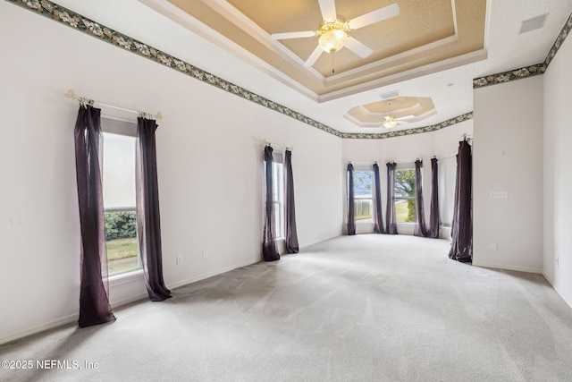 carpeted empty room with ceiling fan, a tray ceiling, visible vents, and baseboards