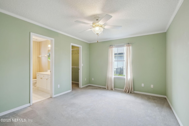 unfurnished bedroom with a textured ceiling, a walk in closet, crown molding, and light colored carpet