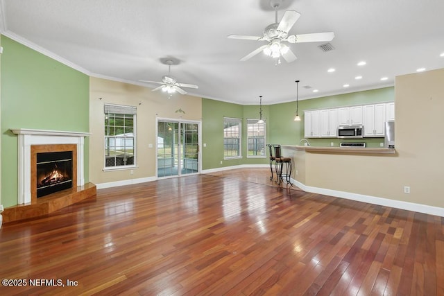 unfurnished living room featuring a healthy amount of sunlight, crown molding, baseboards, and hardwood / wood-style floors