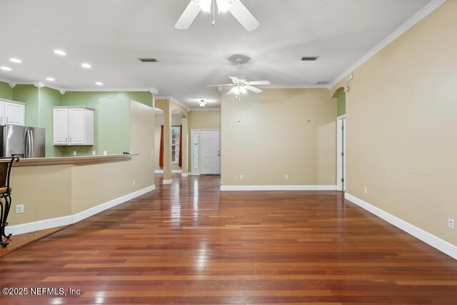 unfurnished living room with visible vents, crown molding, baseboards, and wood finished floors