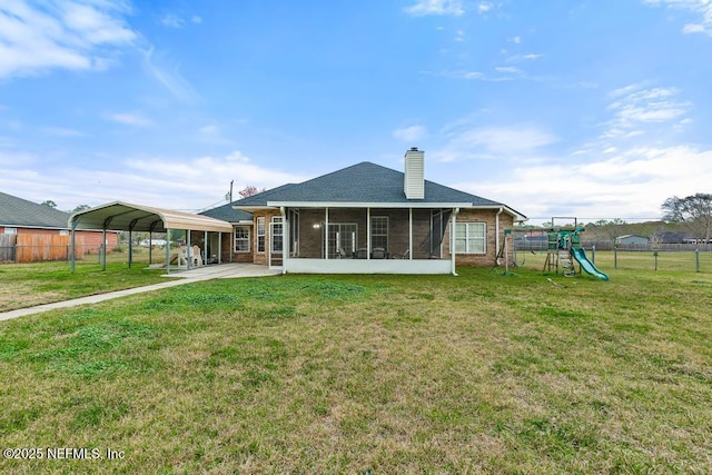 back of house featuring brick siding, fence, a lawn, a detached carport, and a chimney