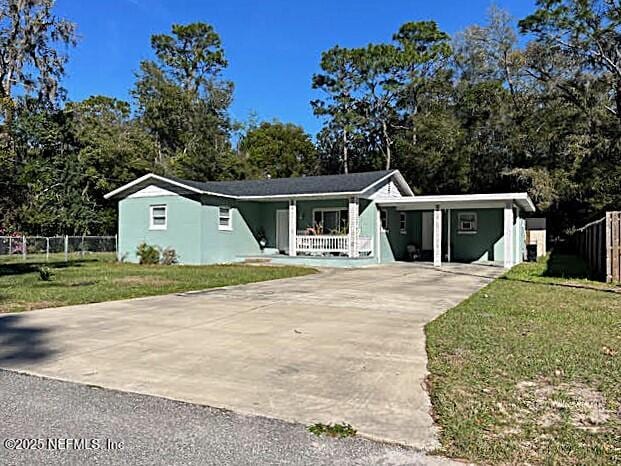 view of front facade with a porch, fence, driveway, stucco siding, and a front lawn