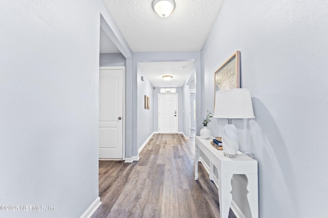 hallway with baseboards, a textured ceiling, and wood finished floors