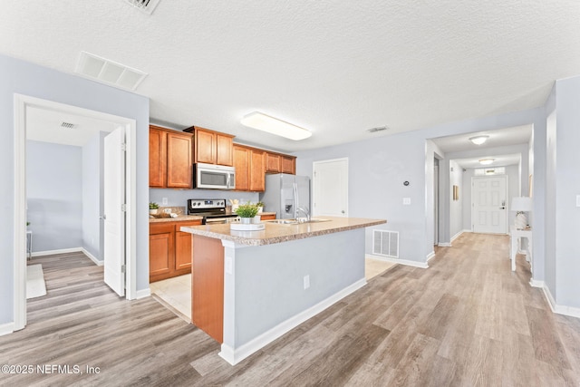 kitchen with stainless steel appliances, an island with sink, and visible vents