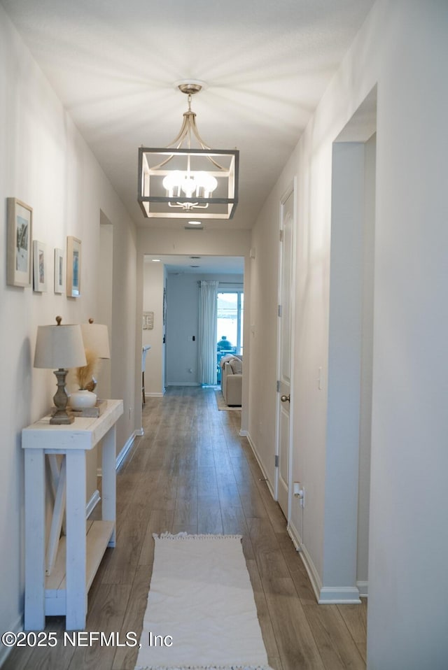 hall with an inviting chandelier, baseboards, and wood finished floors