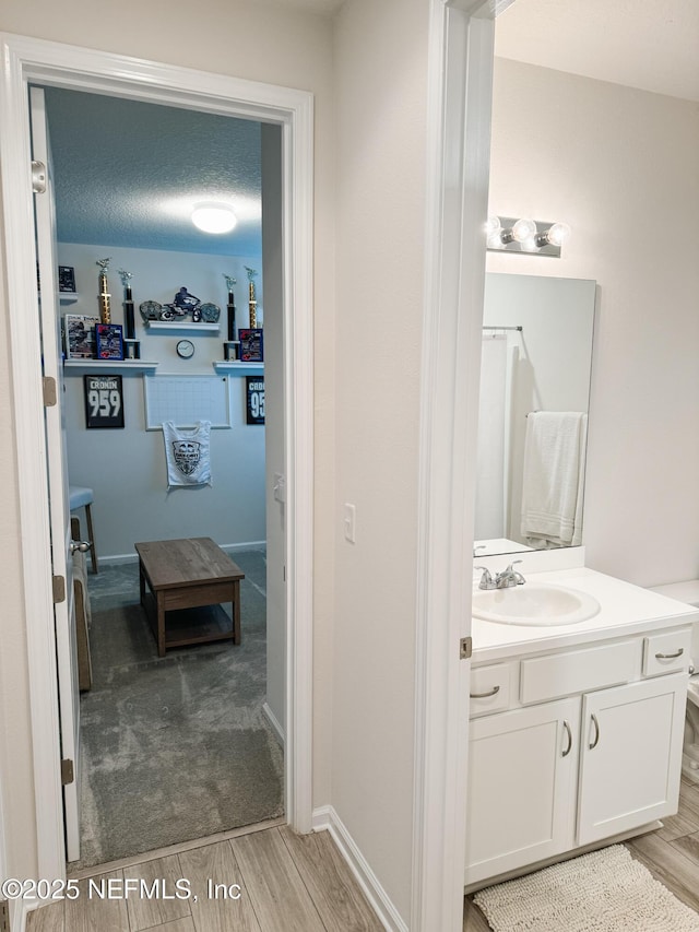 full bathroom with a textured ceiling, wood finish floors, vanity, and baseboards