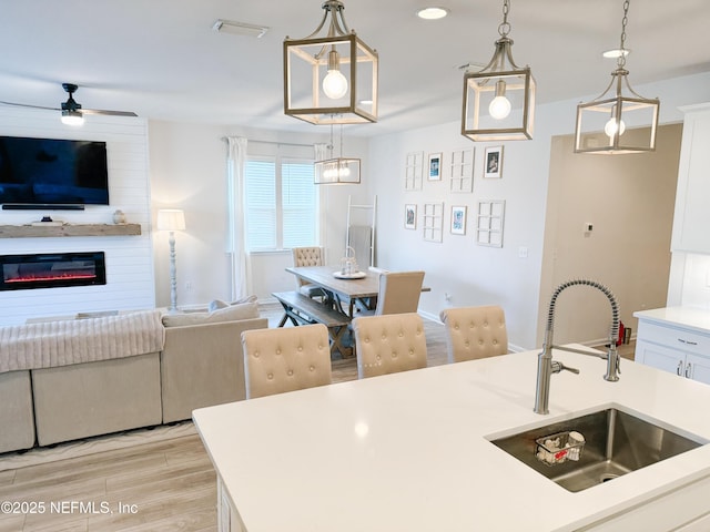 kitchen featuring open floor plan, hanging light fixtures, a sink, and white cabinets