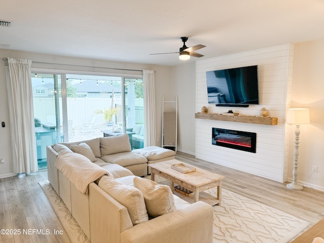 living room featuring visible vents, baseboards, a glass covered fireplace, light wood-style flooring, and ceiling fan