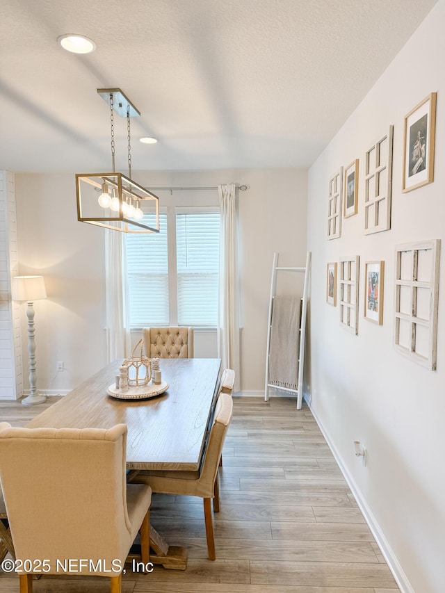 dining area featuring light wood finished floors, baseboards, and a textured ceiling