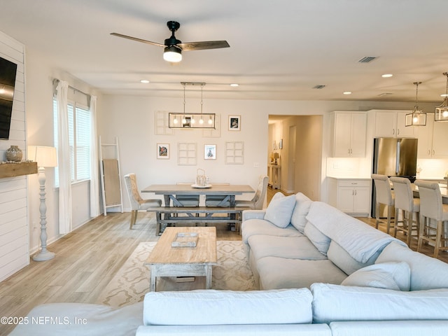 living area featuring light wood finished floors, ceiling fan with notable chandelier, visible vents, and recessed lighting