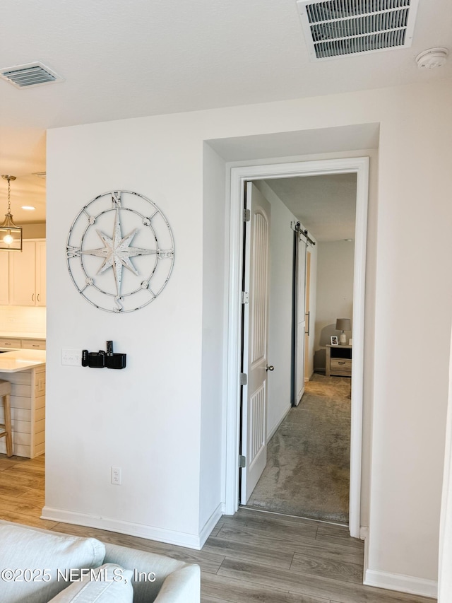 corridor featuring wood finished floors, visible vents, and a barn door