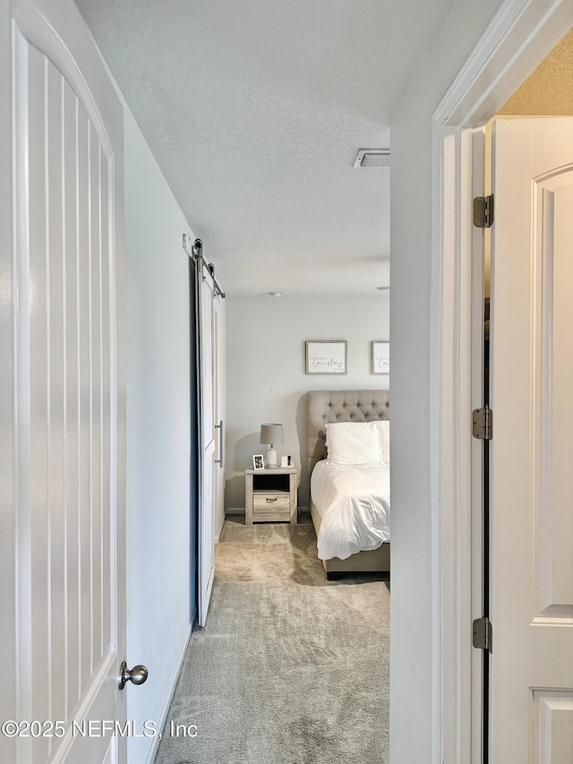 bedroom with a textured ceiling, a barn door, and light colored carpet