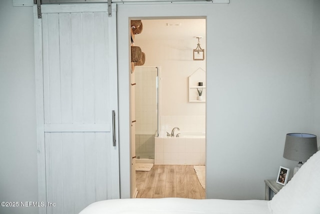 bedroom with ensuite bathroom, a barn door, and wood finished floors