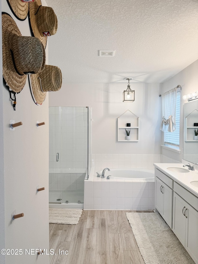 bathroom featuring a textured ceiling, a sink, wood finished floors, visible vents, and a shower stall