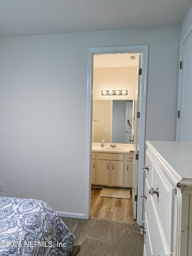 bedroom featuring light carpet, baseboards, ensuite bathroom, light wood-type flooring, and a sink