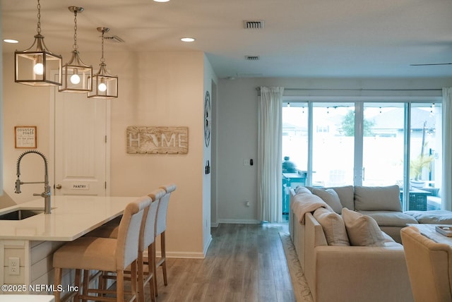 interior space featuring a breakfast bar area, light countertops, hanging light fixtures, open floor plan, and a sink