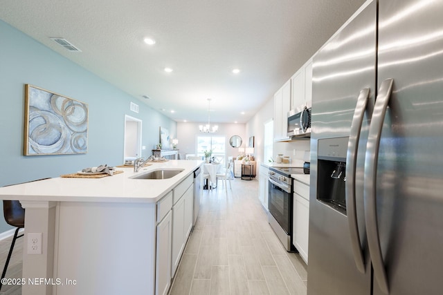 kitchen featuring a kitchen island with sink, appliances with stainless steel finishes, white cabinets, and a sink