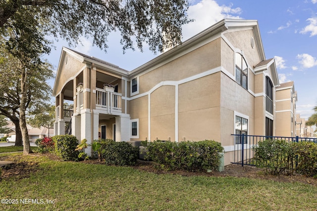 exterior space featuring a balcony, stucco siding, fence, and a yard