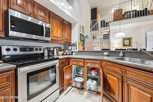 kitchen featuring brown cabinetry, dark countertops, a towering ceiling, appliances with stainless steel finishes, and a sink