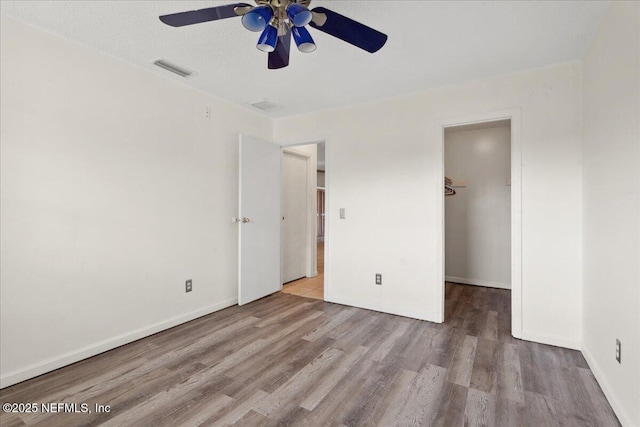 unfurnished bedroom with baseboards, visible vents, a ceiling fan, wood finished floors, and a spacious closet