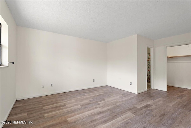 unfurnished bedroom with a closet, a textured ceiling, baseboards, and wood finished floors