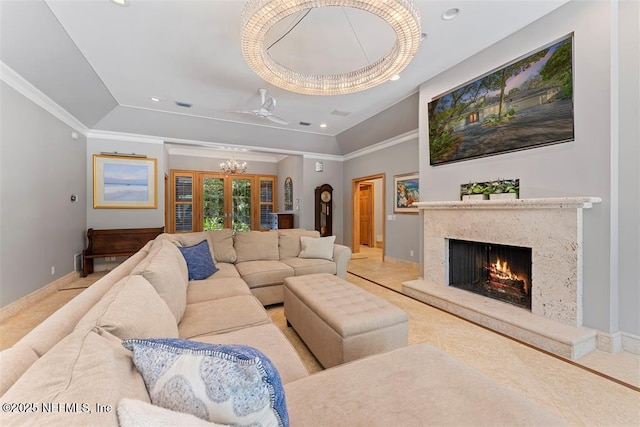 living room featuring a raised ceiling, ornamental molding, a high end fireplace, baseboards, and a chandelier