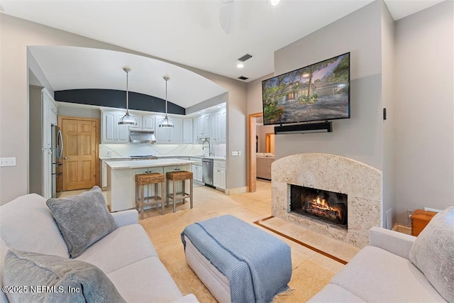living room with visible vents, a ceiling fan, a premium fireplace, baseboards, and vaulted ceiling