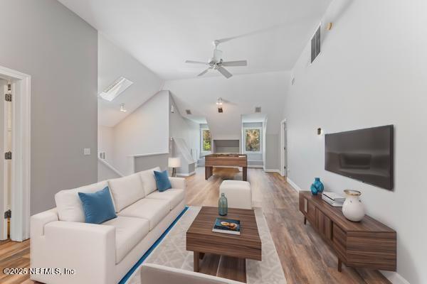 living area with wood finished floors, baseboards, a ceiling fan, visible vents, and vaulted ceiling