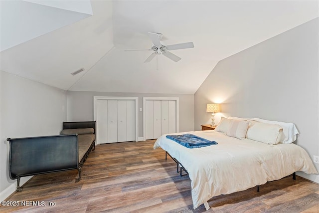 bedroom with wood finished floors, visible vents, ceiling fan, vaulted ceiling, and two closets