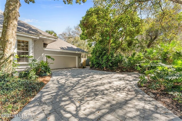 view of property exterior featuring a garage, roof with shingles, and driveway
