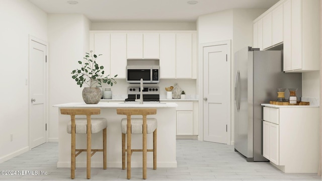 kitchen featuring an island with sink, a breakfast bar area, stainless steel appliances, light countertops, and white cabinetry