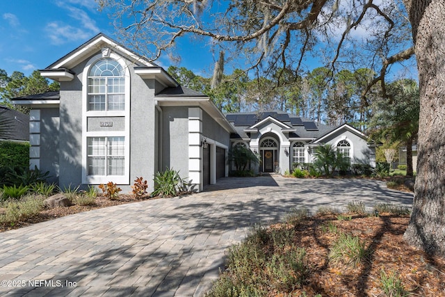 traditional home featuring a garage, decorative driveway, roof mounted solar panels, and stucco siding