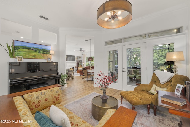 living room featuring ceiling fan with notable chandelier, wood finished floors, visible vents, french doors, and crown molding