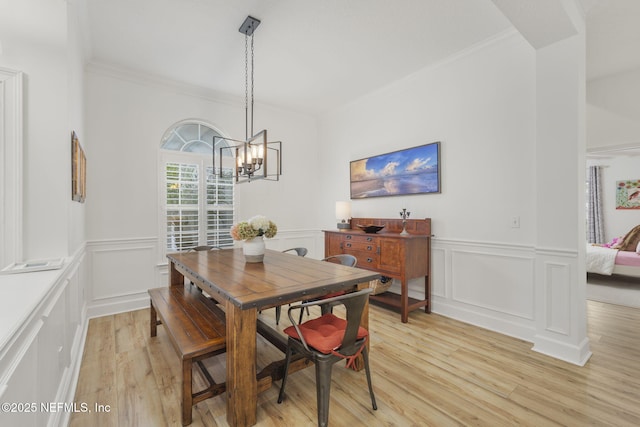 dining room featuring ornamental molding, a decorative wall, light wood-style flooring, and an inviting chandelier