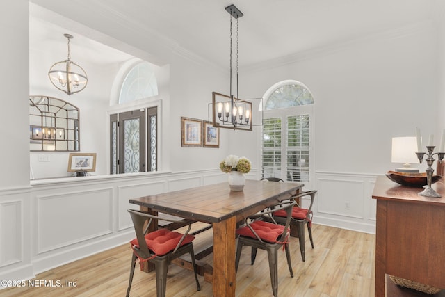 dining room with an inviting chandelier, light wood-style flooring, ornamental molding, and a wainscoted wall