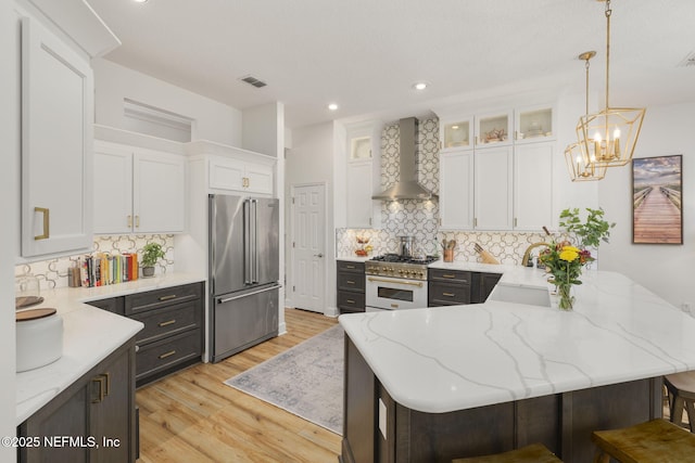 kitchen with a peninsula, a sink, high quality appliances, white cabinets, and wall chimney range hood