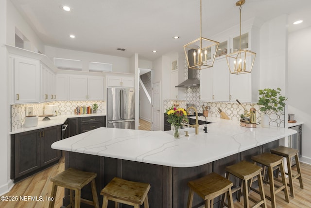 kitchen featuring high end fridge, white cabinetry, a peninsula, and wall chimney exhaust hood