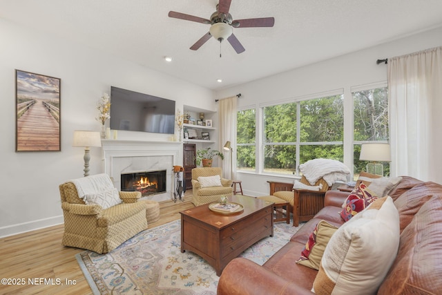 living area with ceiling fan, a fireplace, baseboards, and wood finished floors