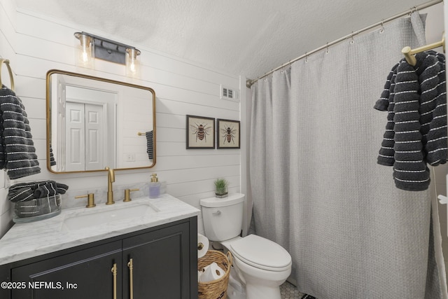 full bath with a textured ceiling, toilet, wood walls, vanity, and visible vents